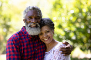 portrait of a senior mixed race couple enjoying their time at the garden, embracing, looking at the camera and smiling, on a sunny day
